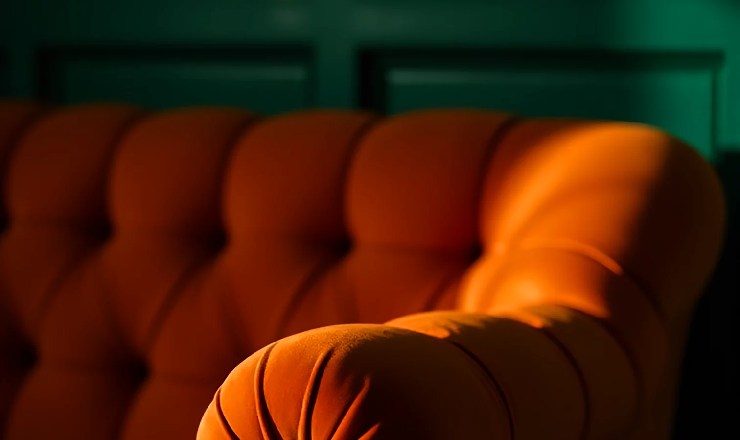 An orange velvet sofa against a dark green wall